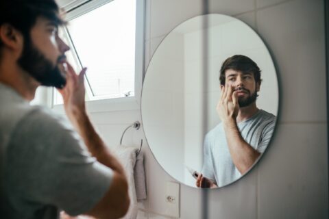 A man is applying skincare product in front of a bathroom mirror in Dallas, TX, and surrounding area